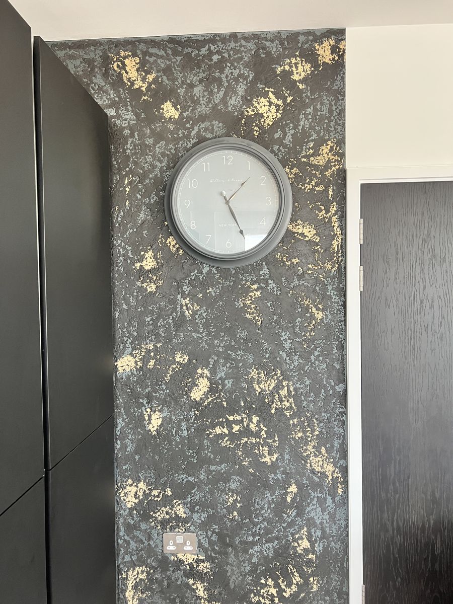 Black plaster wall with gold leaf detail and a clock